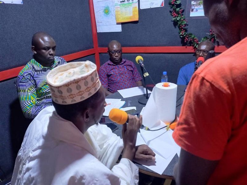 Men speak into microphones sitting around a table at a radio station